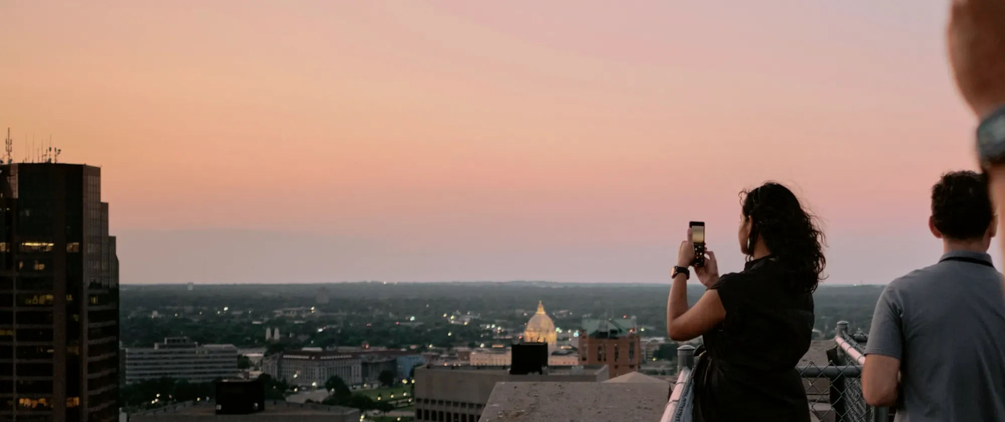 Guests on a downtown rooftop photographing the Saint Paul skyline at sunset